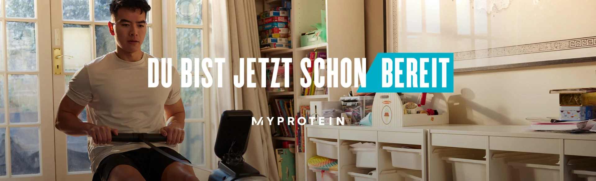 A man workout out on a rowing machine at home with the words 'You're Already Ready - MYPROTEIN' overlaying.