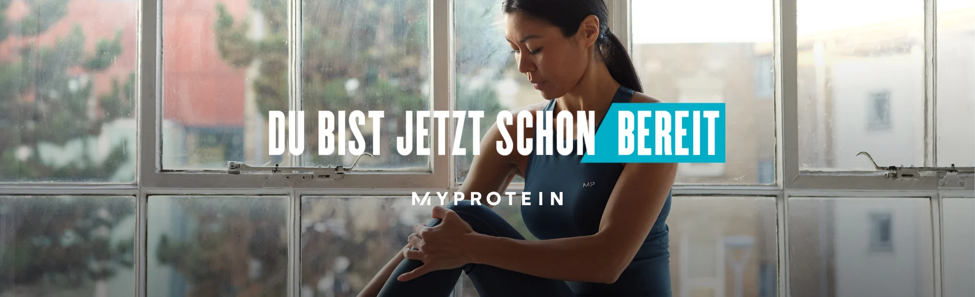 A woman wearing MP gym clothing sat on a window ledge stretching with the text 'You're Already Ready - MYPROTEIN' overlaying the image.